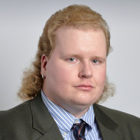 Teemu Lähde 2.3.2023. Kuvaaja: Earl Richardson. Paikka: Stauffer-Flint Hall, 3. kerros, Kansasin yliopiston kampus. Teemu Lähde ammattimaisessa lähikuvassa pukeutuneena pikkutakkiin ja solmioon.